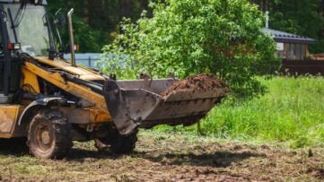Equipamentos pesados realizando a limpeza de terreno, removendo detritos e vegetação.